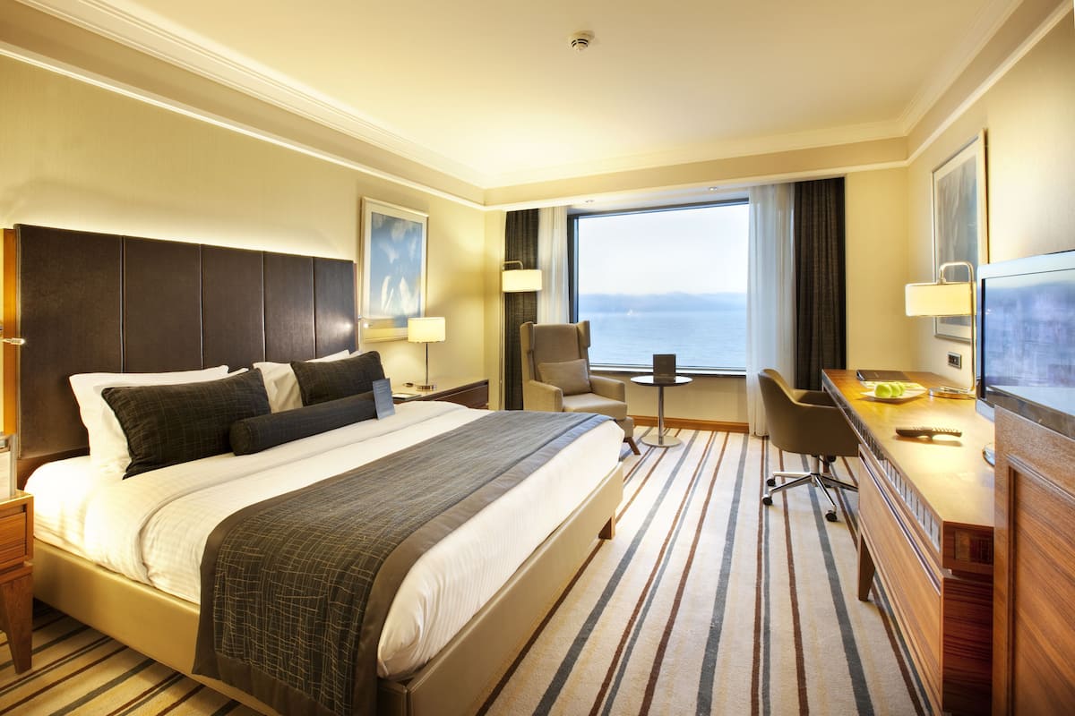 A hotel room with a large bed, a desk, a chair, and a view of the sea.