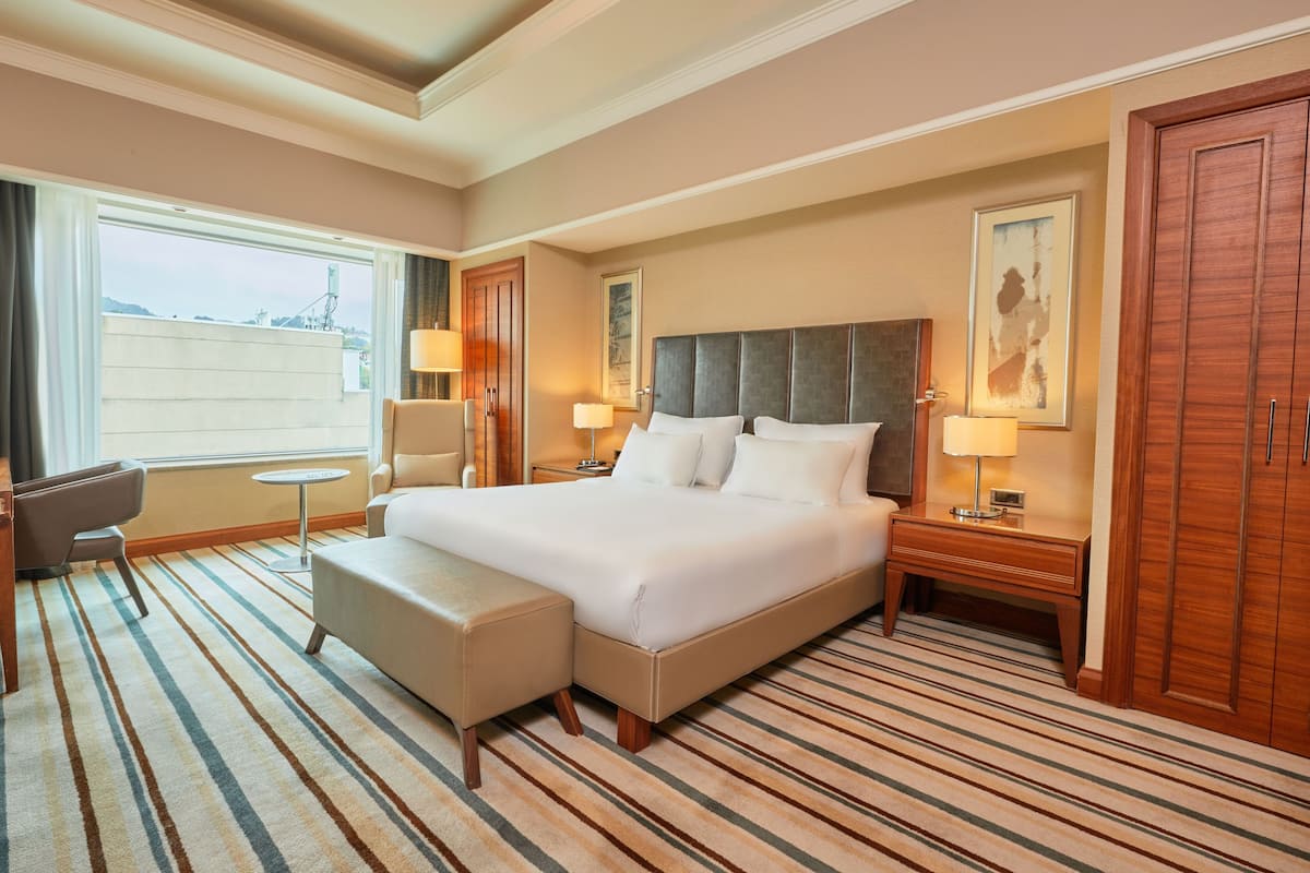 A hotel room with a large bed, a desk, a chair, and a small table.