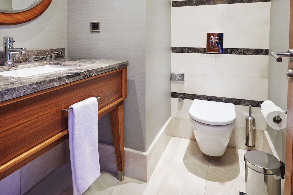 A modern bathroom with a marble sink, a wooden vanity, a toilet, and a trash can.