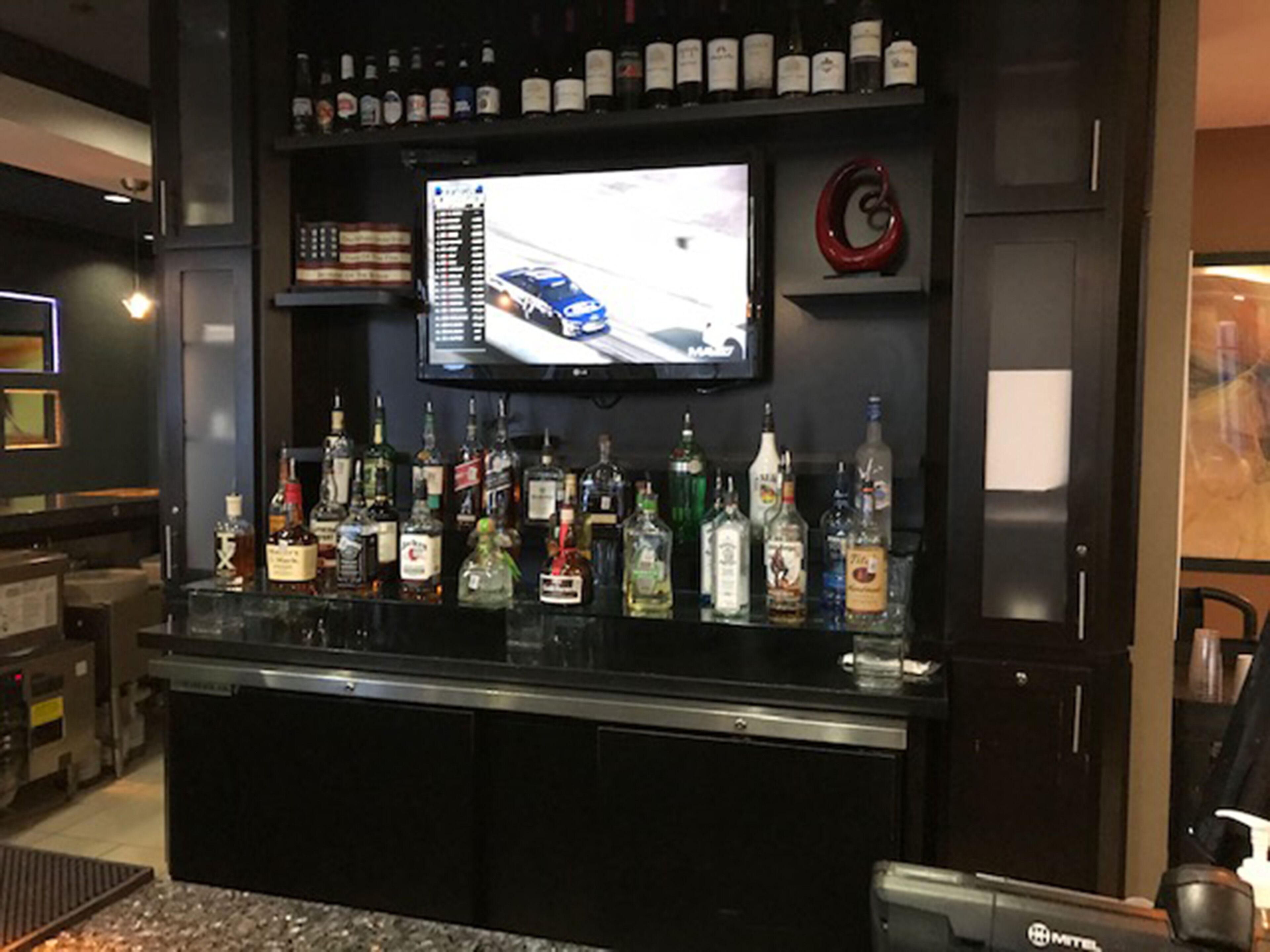 Un coin bar avec un téléviseur fixé au-dessus d’une étagère où sont rangées des bouteilles d’alcool.