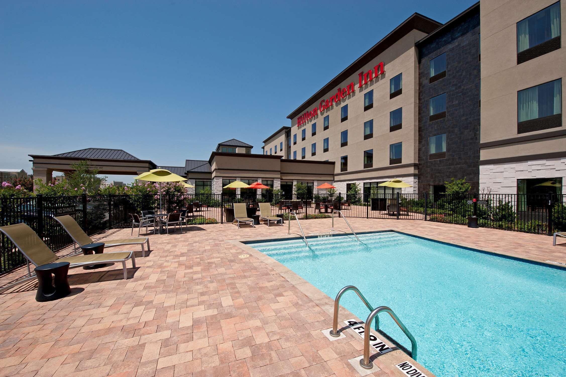 A pool area with lounge chairs and umbrellas, a pool, and a building labeled "Hilton Garden Inn".