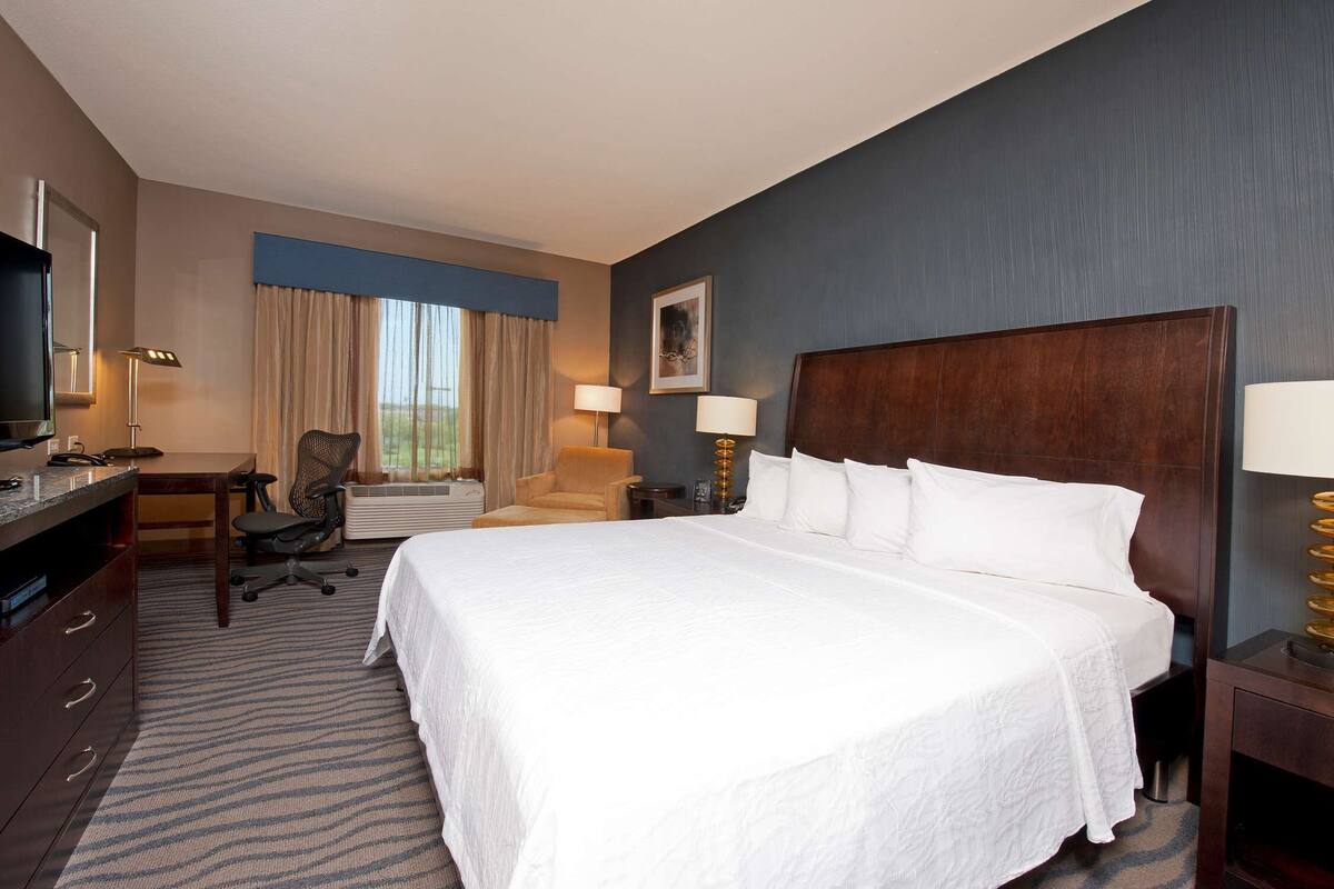Una habitación de hotel con una cama grande, un escritorio con silla, un televisor y una ventana con cortinas.