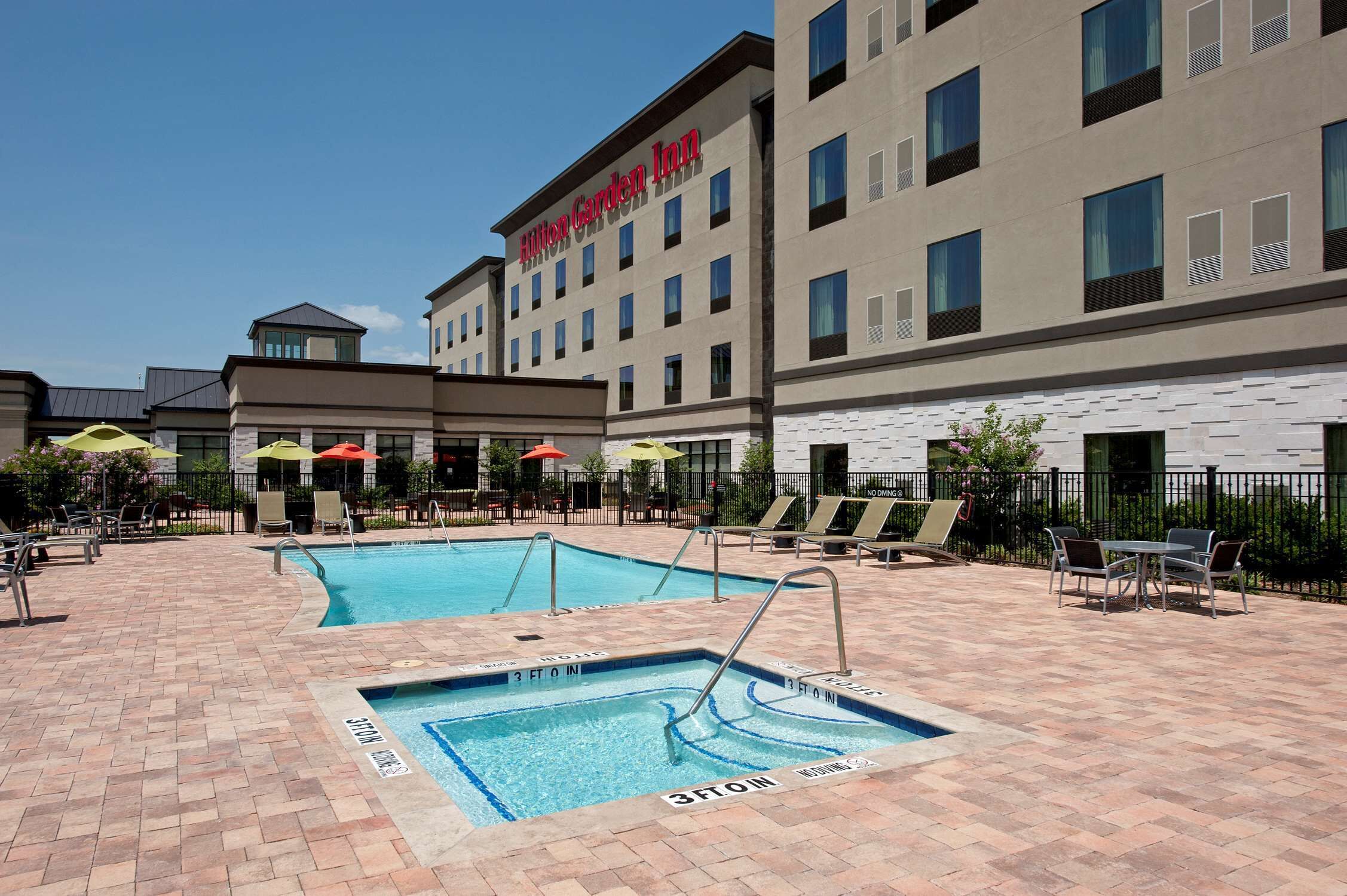 A hotel with a swimming pool, outdoor seating, and umbrellas.