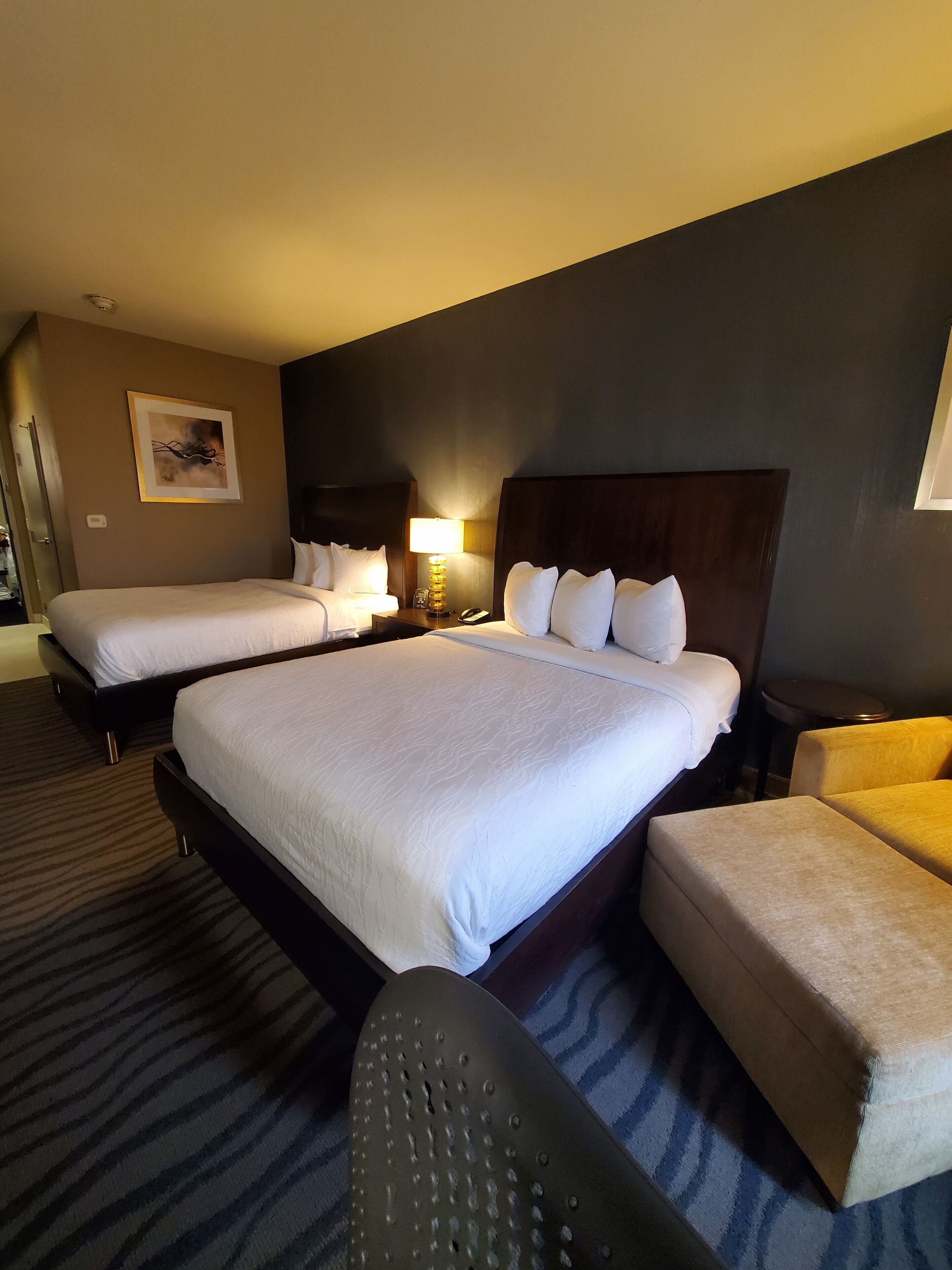Une chambre d’hôtel avec deux lits, une table de chevet avec une lampe, une chaise et une petite table ronde.
