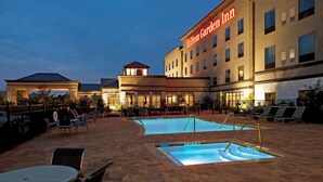 Un hotel con piscina, mobiliario exterior y un edificio grande con un cartel.