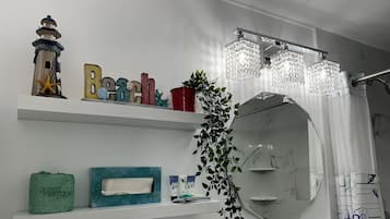 Un baño con lavamanos de mármol, un espejo grande, una planta colgante y un estante con artículos de tocador.