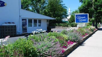 A motel with a signboard, a flower bed, and a church in the background.