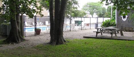 Patio trasero cercado con piscina, mesa de picnic y árboles.