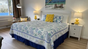 A bedroom with a bed, two bedside tables, a nightstand, a window, and a painting of a beach scene.