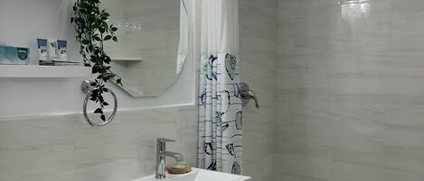A modern bathroom with a white sink, toilet, and shower. There is a mirror above the sink and a plant hanging on the wall.