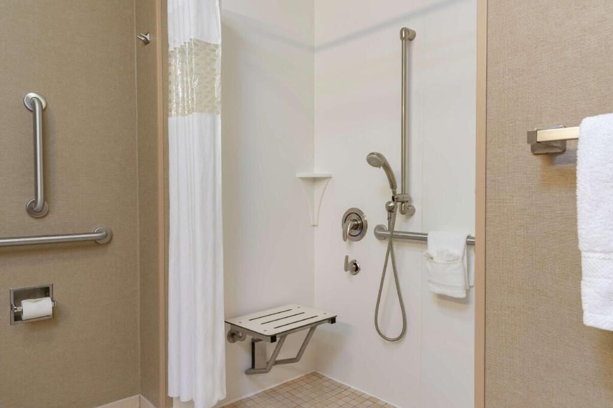 A shower with a handheld showerhead, a handheld showerhead, a towel rack, and a grab bar.