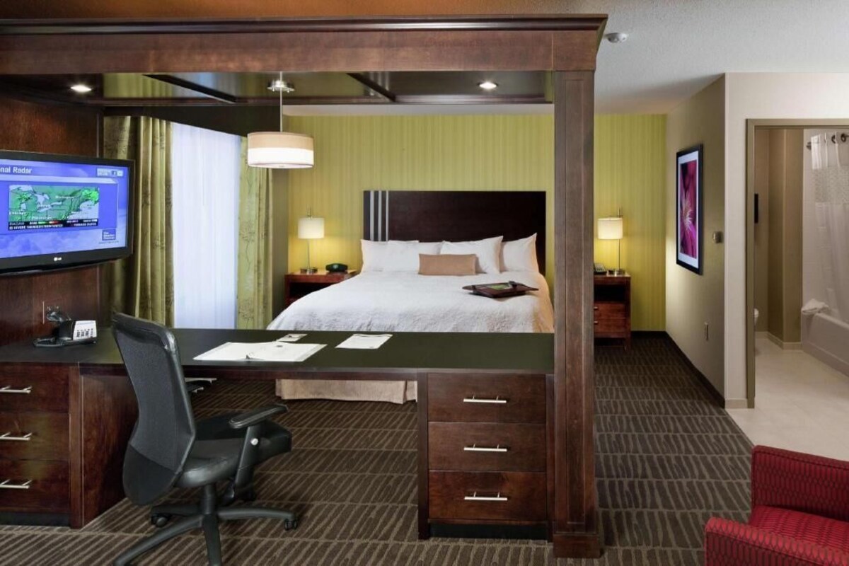 A hotel room with a bed, desk, chair, TV, and a red sofa.