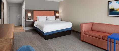 A hotel room with a bed, a desk, a chair, a sofa, and a wall-mounted painting.