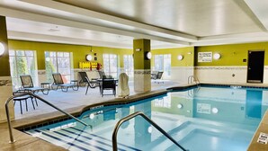 An indoor swimming pool with clear blue water, surrounded by lounge chairs and a sunbed.