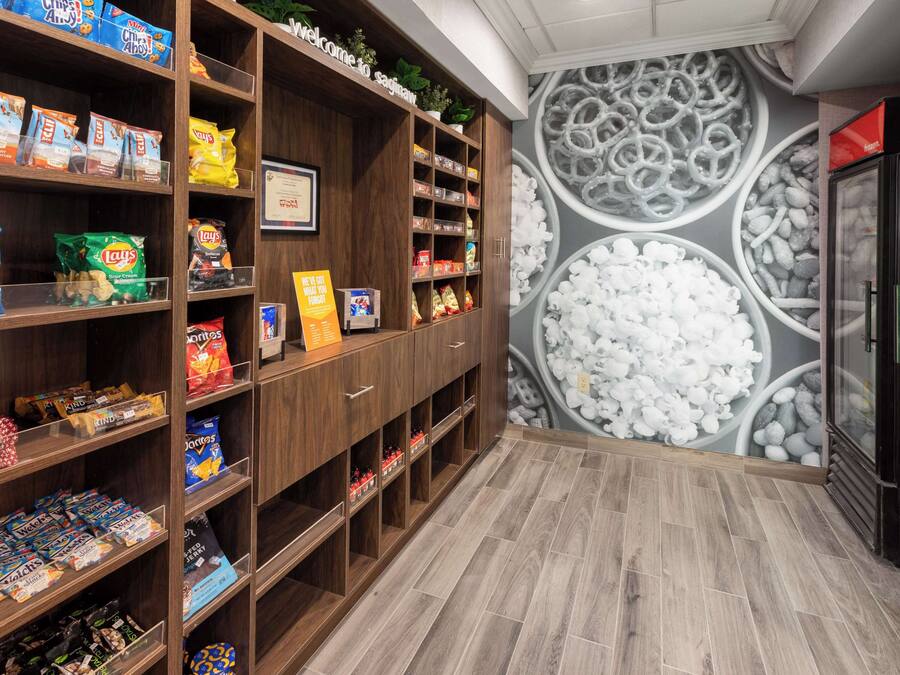 A snack aisle with various chips and snacks, a welcome sign, and a mural of food items on the wall.
