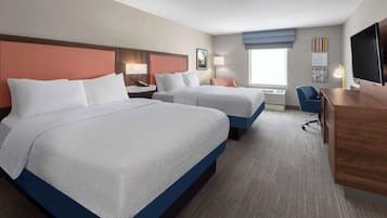 A hotel room with two beds, a desk, a chair, a TV, and artwork on the walls.
