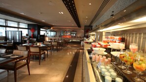 A modern hotel lobby with a buffet area, seating arrangements, and a view of the cityscape through large windows.