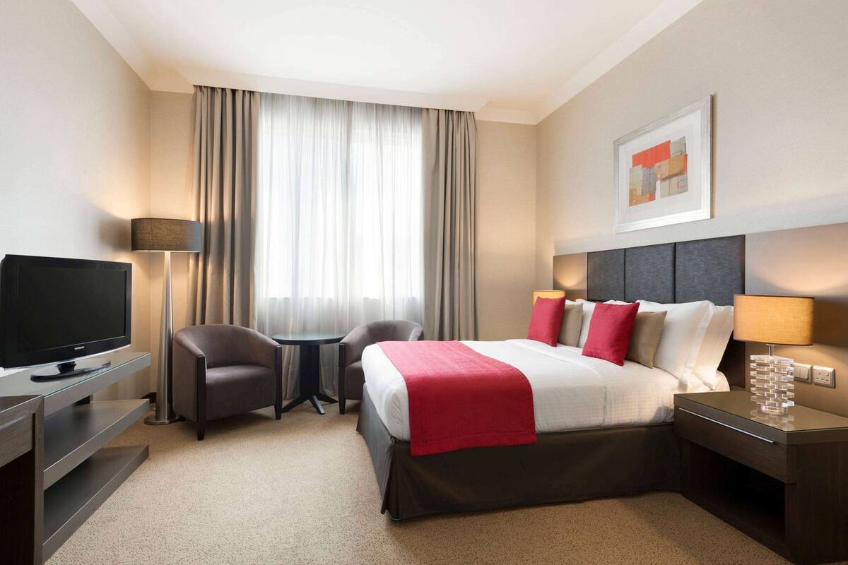 Ein Hotelzimmer mit Bett, Fernseher, Schreibtisch, Stuhl und Lampe.