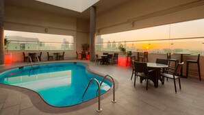 An indoor swimming pool with a view of the sunset, surrounded by tables and chairs. - Ramada by Wyndham Abu Dhabi Downtown (Abu Dhabi)