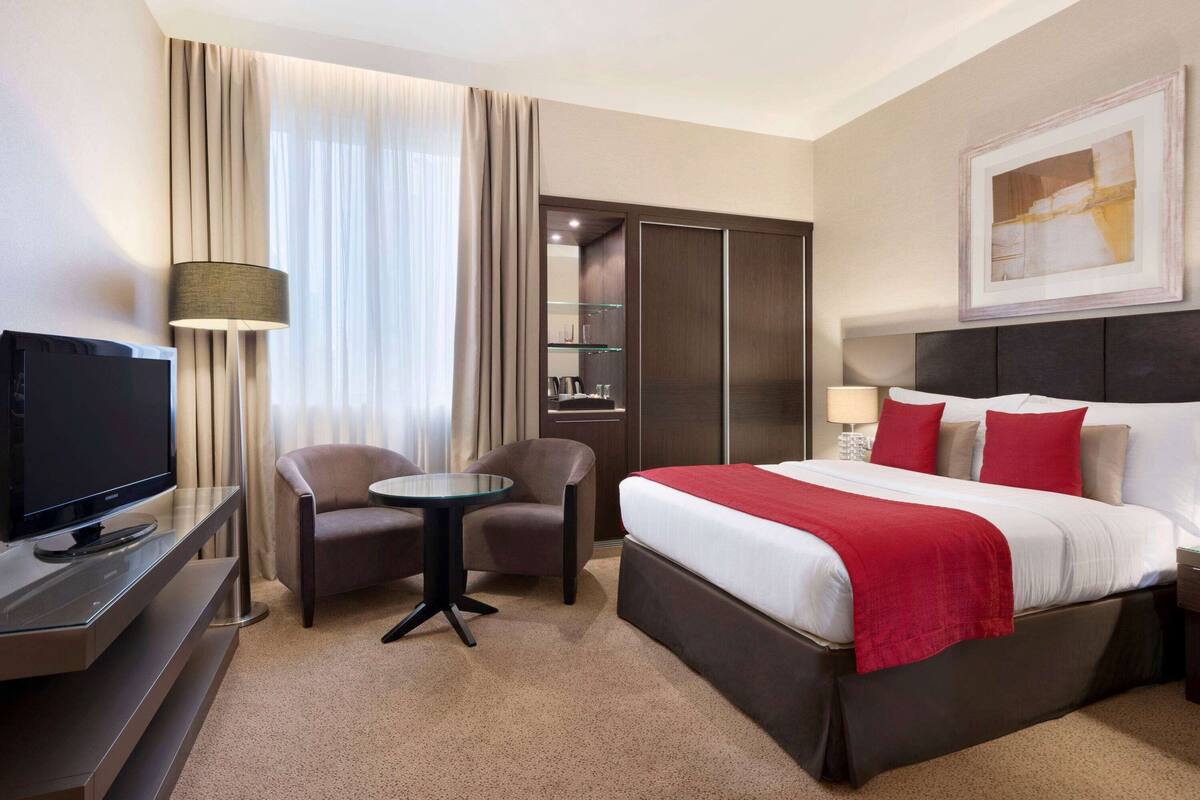 Ein Hotelzimmer mit Bett, Fernseher, Schreibtisch, Stuhl, einem kleinen Tisch und einem Kleiderschrank.