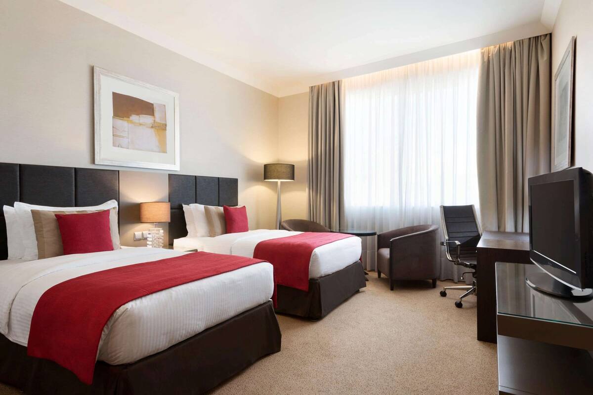 Ein Hotelzimmer mit zwei Betten, einem Schreibtisch, einem Stuhl, einem Fernseher und einer Lampe.