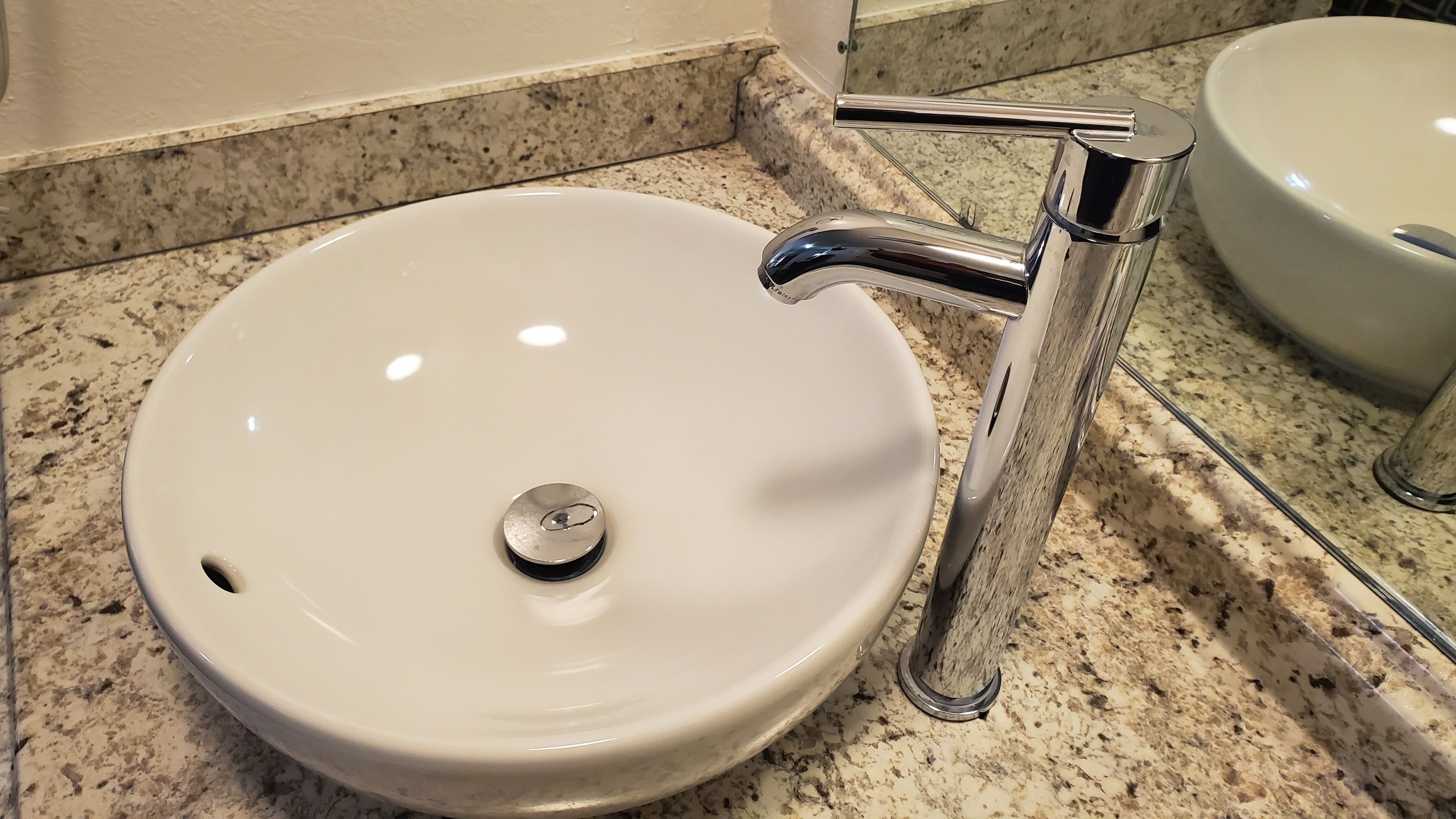 A white sink with a chrome faucet and a round drain, set on a speckled granite countertop.
