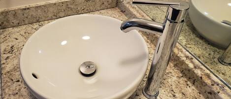 A white sink with a chrome faucet and a round drain, set on a speckled granite countertop.