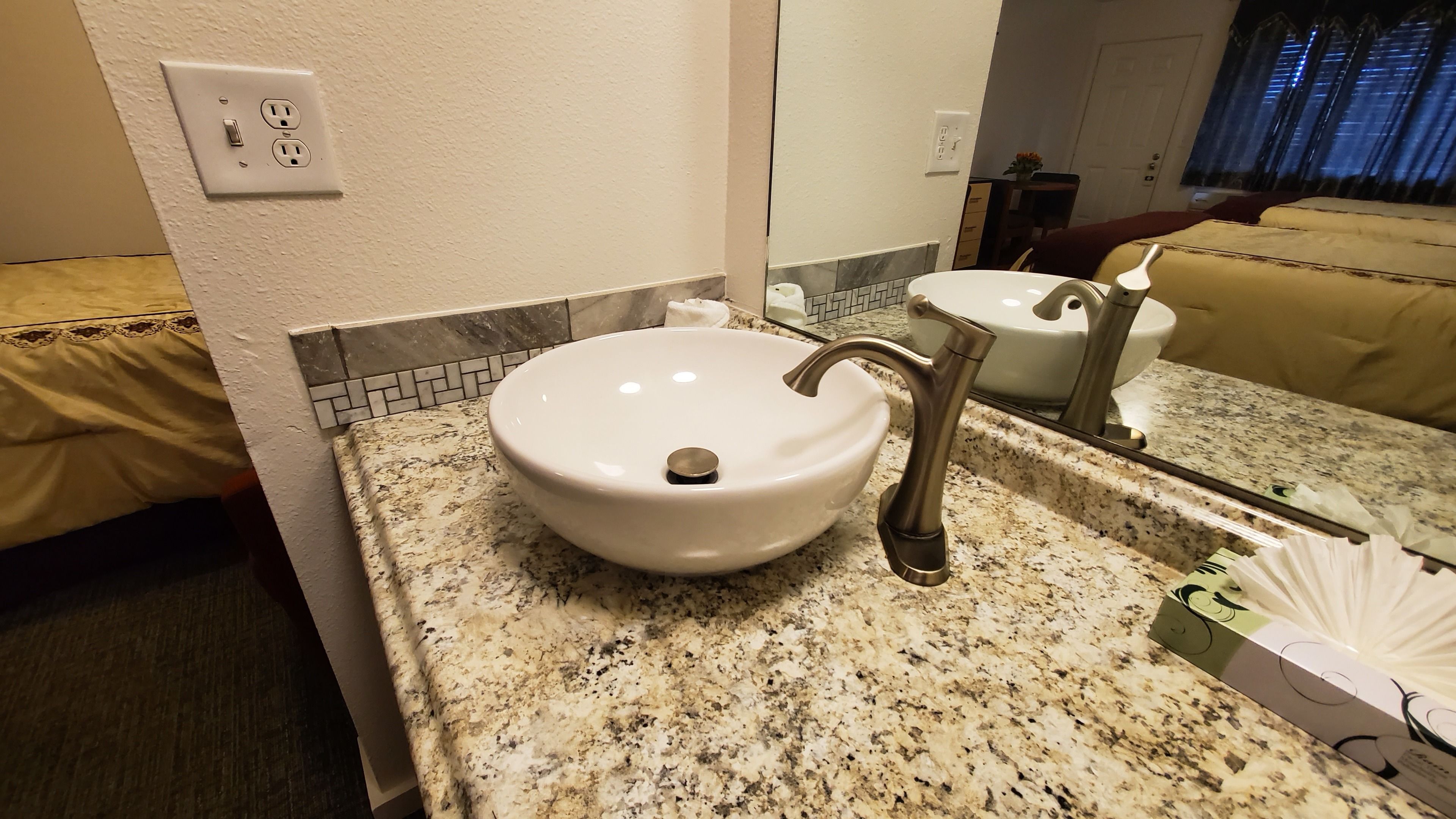 Un baño con lavamanos blanco, un espejo y encimera de granito.