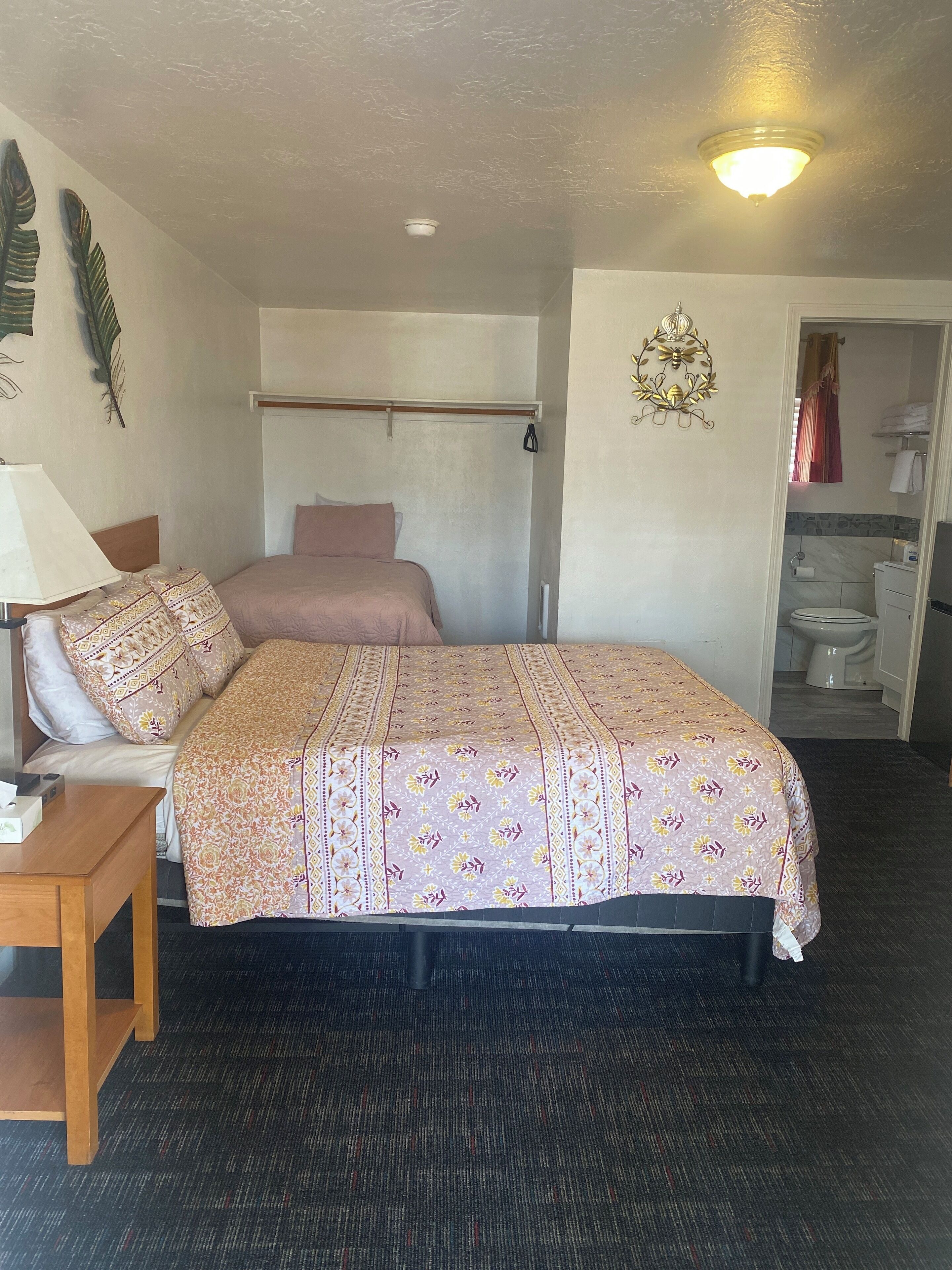 A bedroom with a bed, bedside table, lamp, and a view into the bathroom.