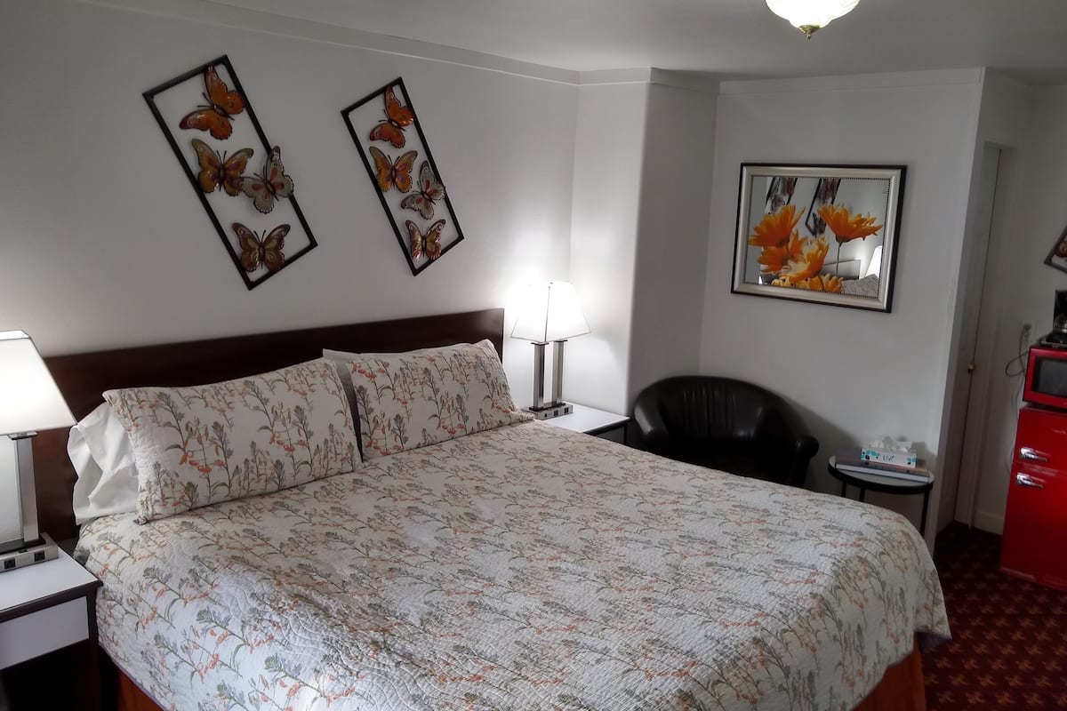 Una camera d'albergo con un letto, una scrivania con una lampada, una sedia e opere d'arte alle pareti.