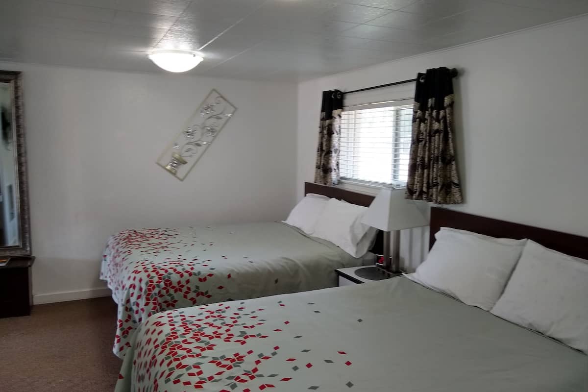 Camera d'albergo con due letti, un comodino, una lampada, una sveglia e una finestra con tende.