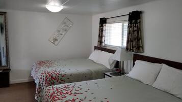Camera d'albergo con due letti, un comodino, una lampada, una sveglia e una finestra con tende.