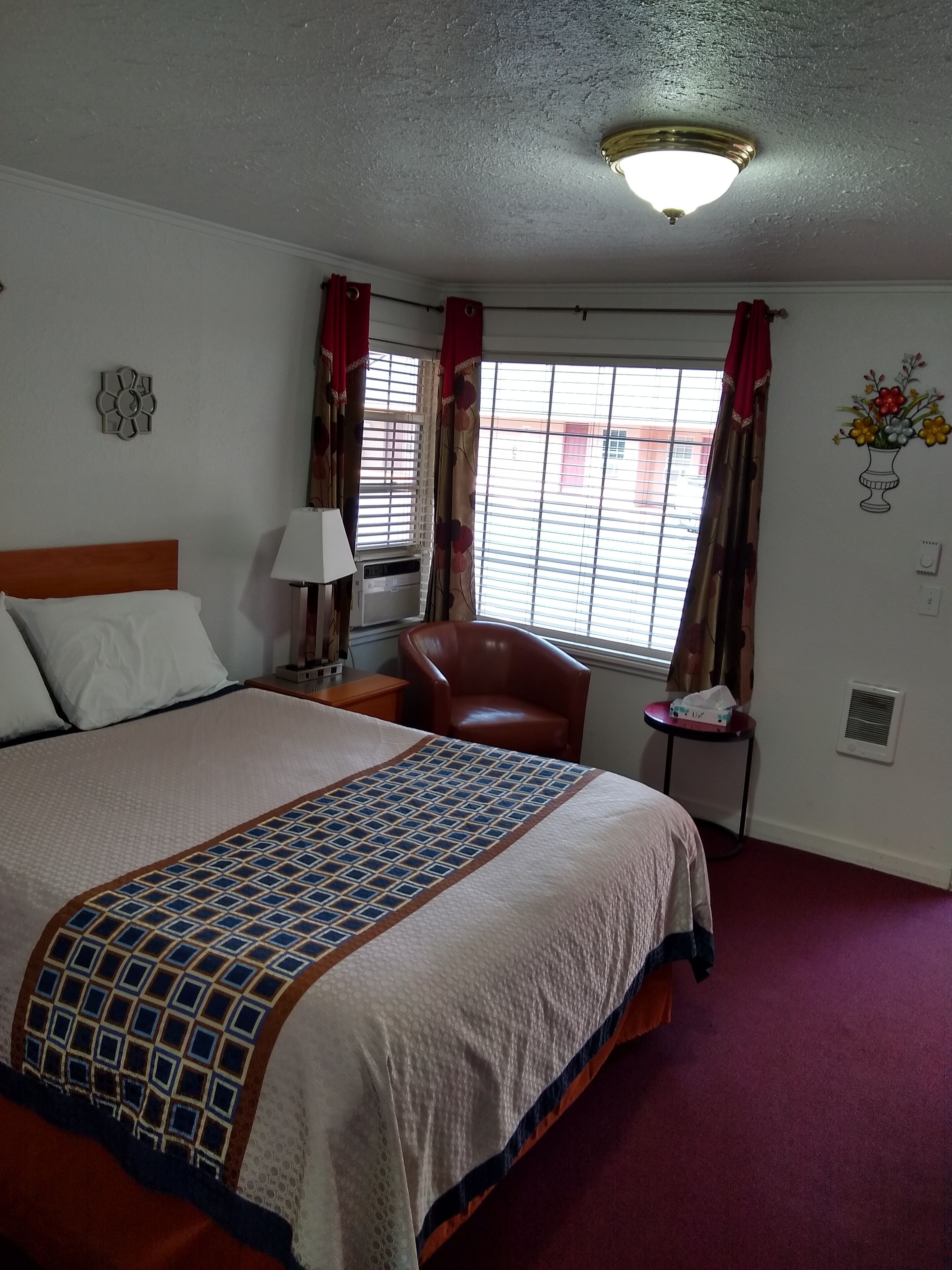 Una habitación de hotel con una cama grande, una silla, una mesita y una ventana con cortinas.