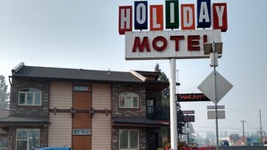 Letrero de Motel Holiday con una bandera, un coche azul estacionado al frente y un edificio con un letrero que dice 'Office'.