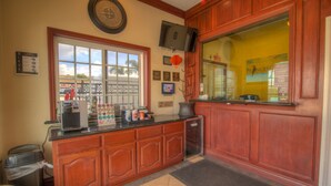A hotel reception area with a wooden counter, a coffee machine, a trash bin, and a large window.