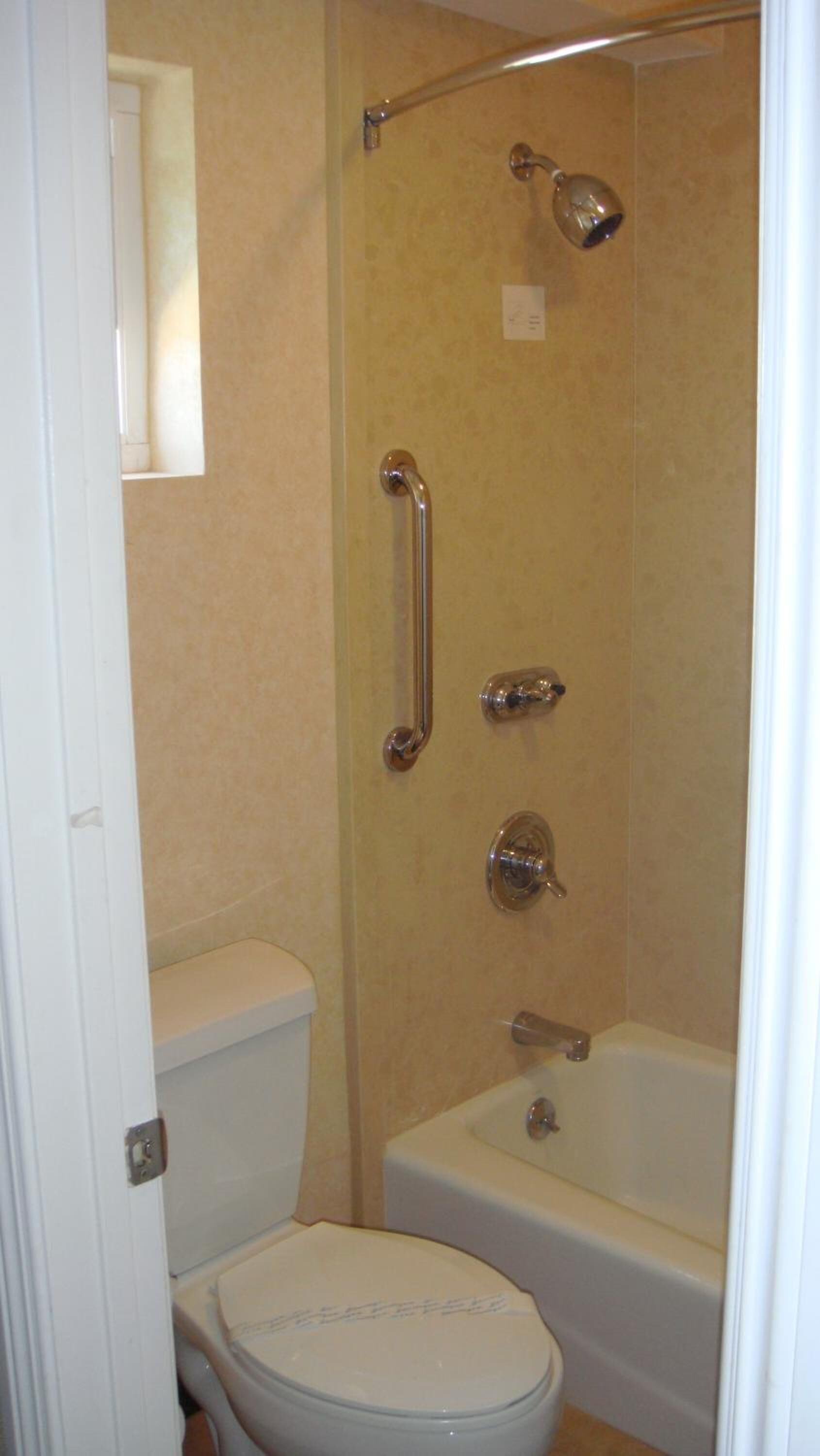 Un baño con inodoro, bañera y ducha con barra de apoyo.
