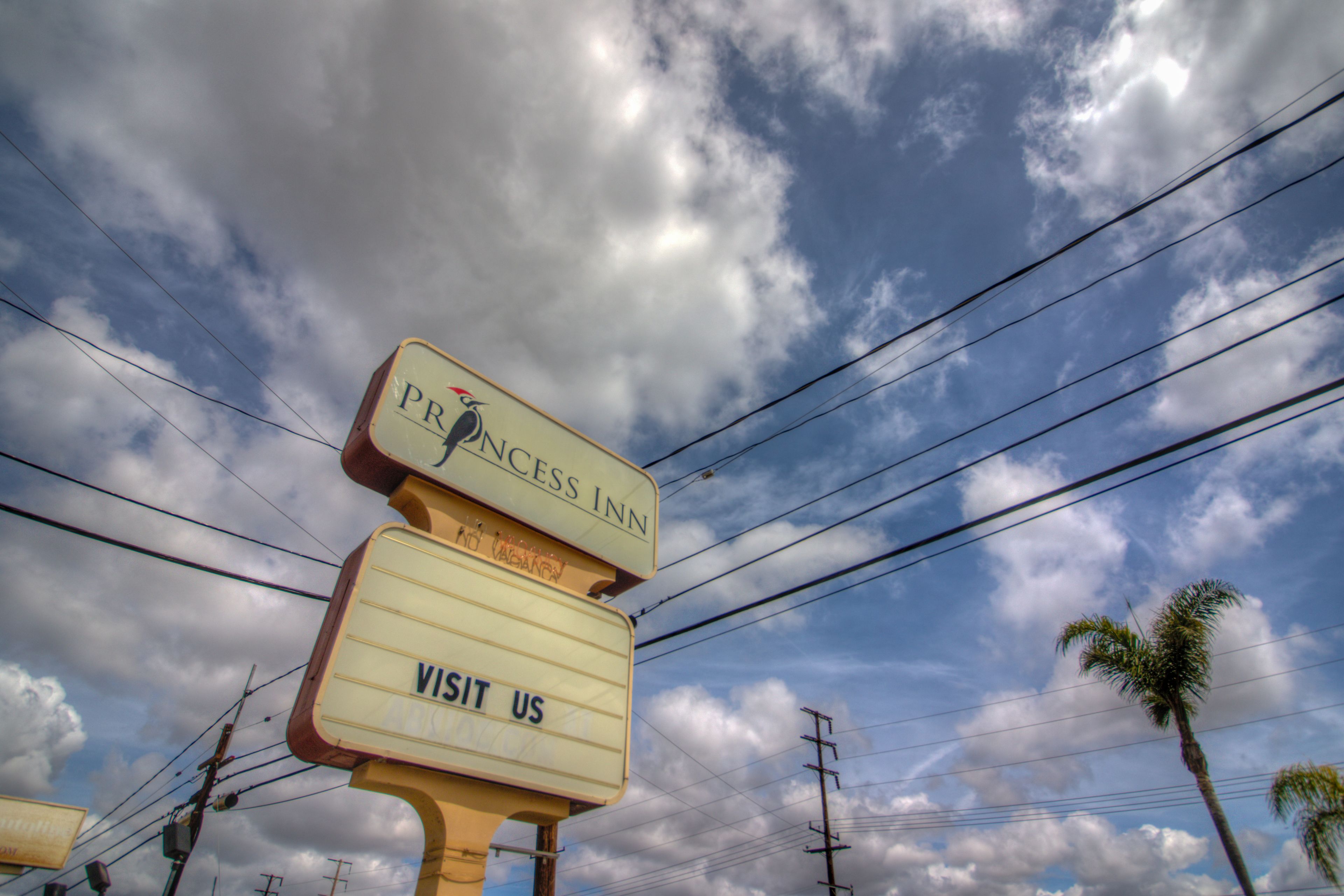 A sign for Princess Inn with a 'VISIT US' prompt, set against a backdrop of power lines and a partly cloudy sky.