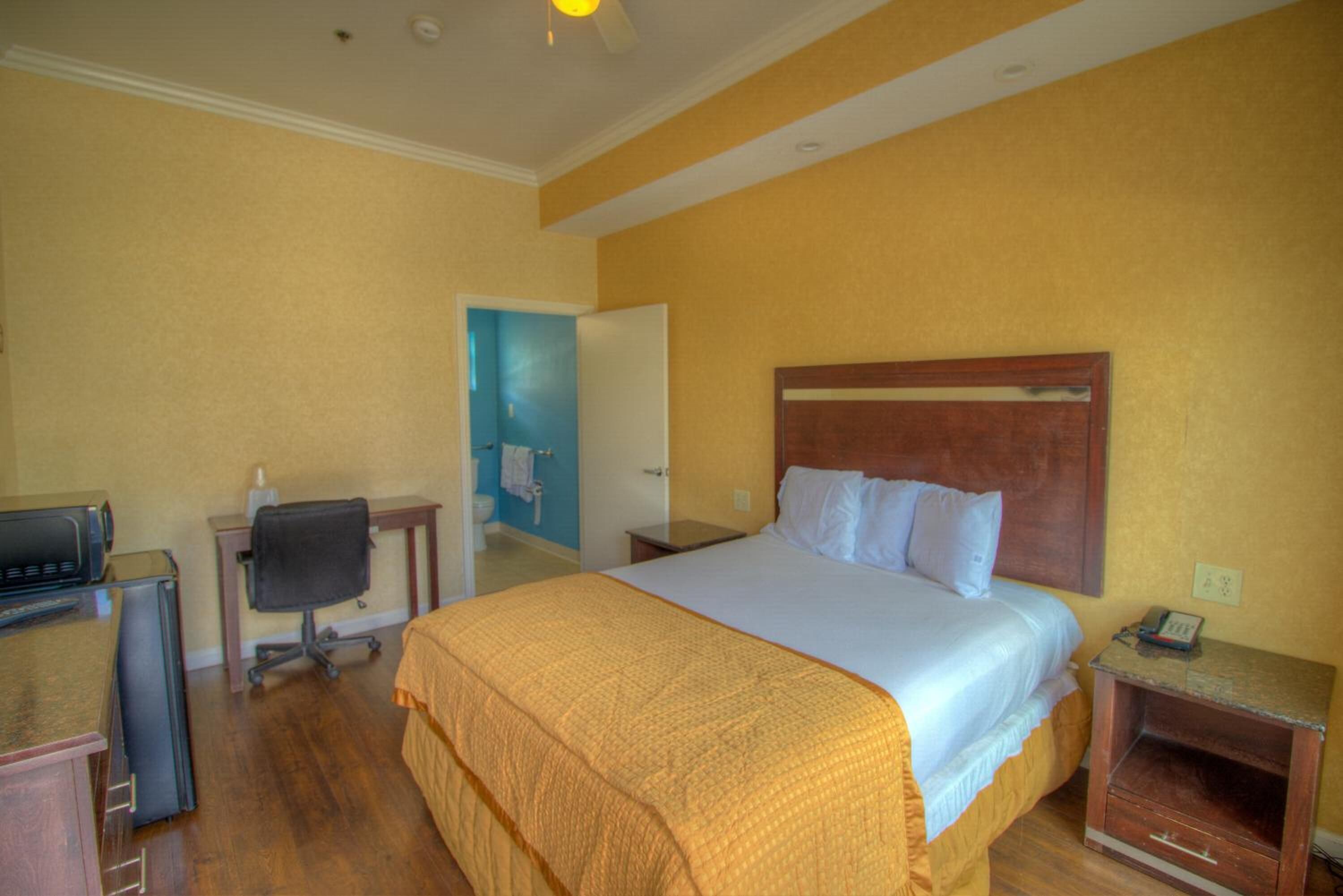 A hotel room with a bed, a desk with a computer, a chair, and a small table with a phone.