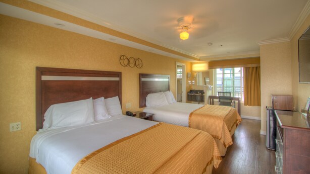 A hotel room with two beds, a desk, a mirror, and a window with curtains.
