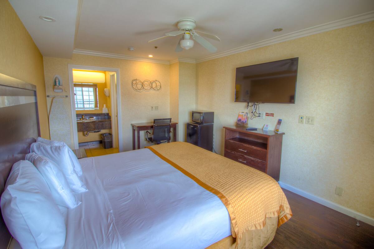 Une chambre d’hôtel avec un lit, un bureau, une télévision et une salle de bain visible à travers une porte ouverte.