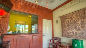 A reception area with a wooden counter, a white door, a patterned tapestry, and a green recycling bin.