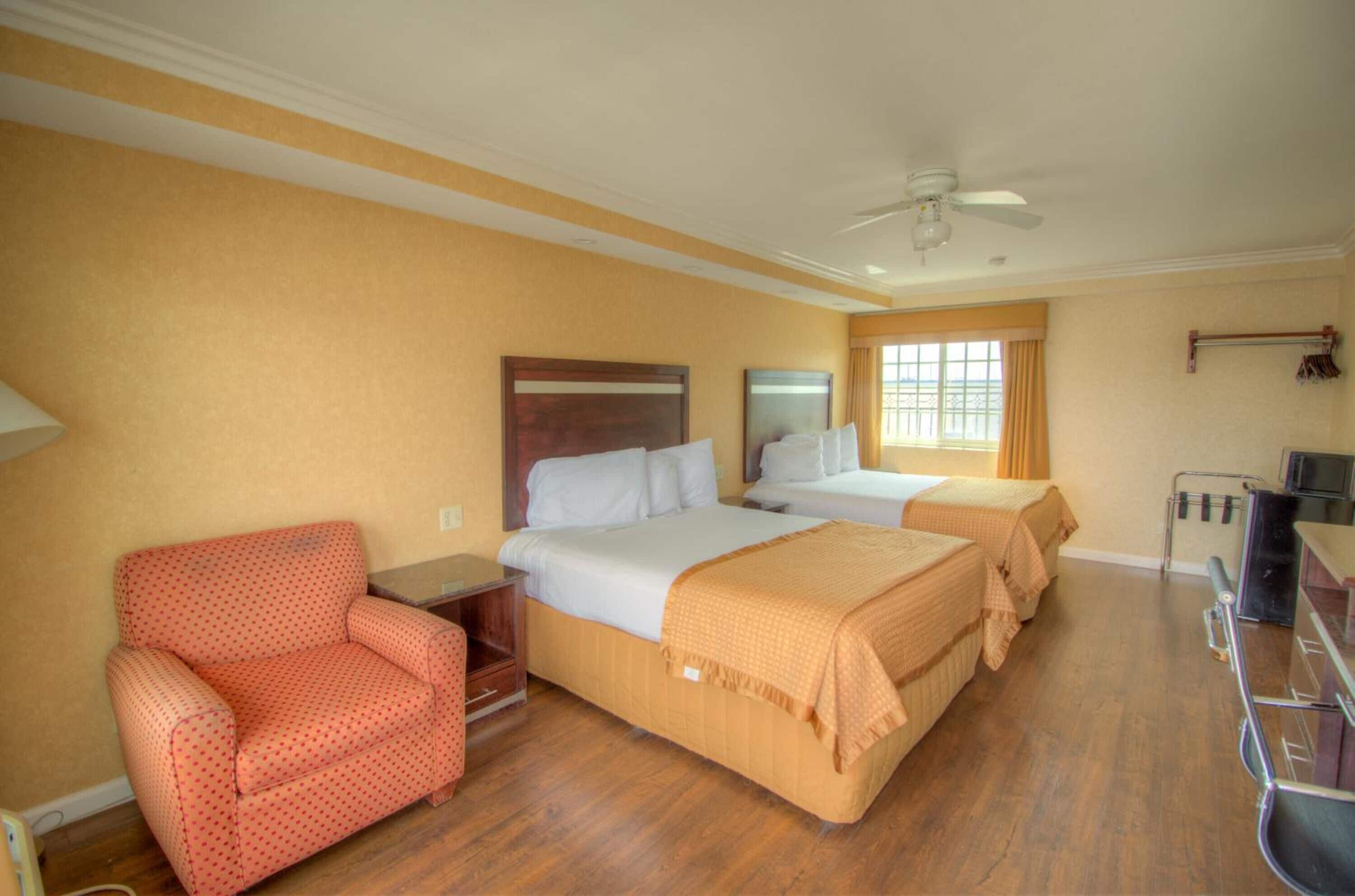 Ein Hotelzimmer mit zwei Betten, einem Sessel, einem Schreibtisch und einem Fenster mit Vorhängen.