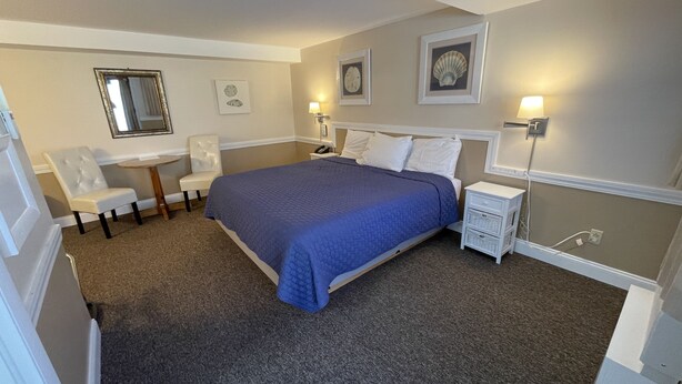A neatly arranged bedroom with a bed, a chair, a small table, and wall-mounted lamps.