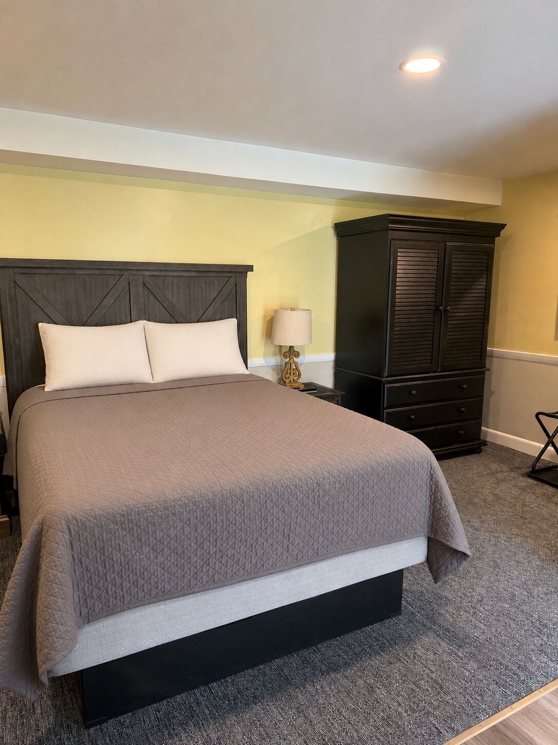 A neatly made bed with a dark headboard, a dark wooden wardrobe, and a lamp on a bedside table.