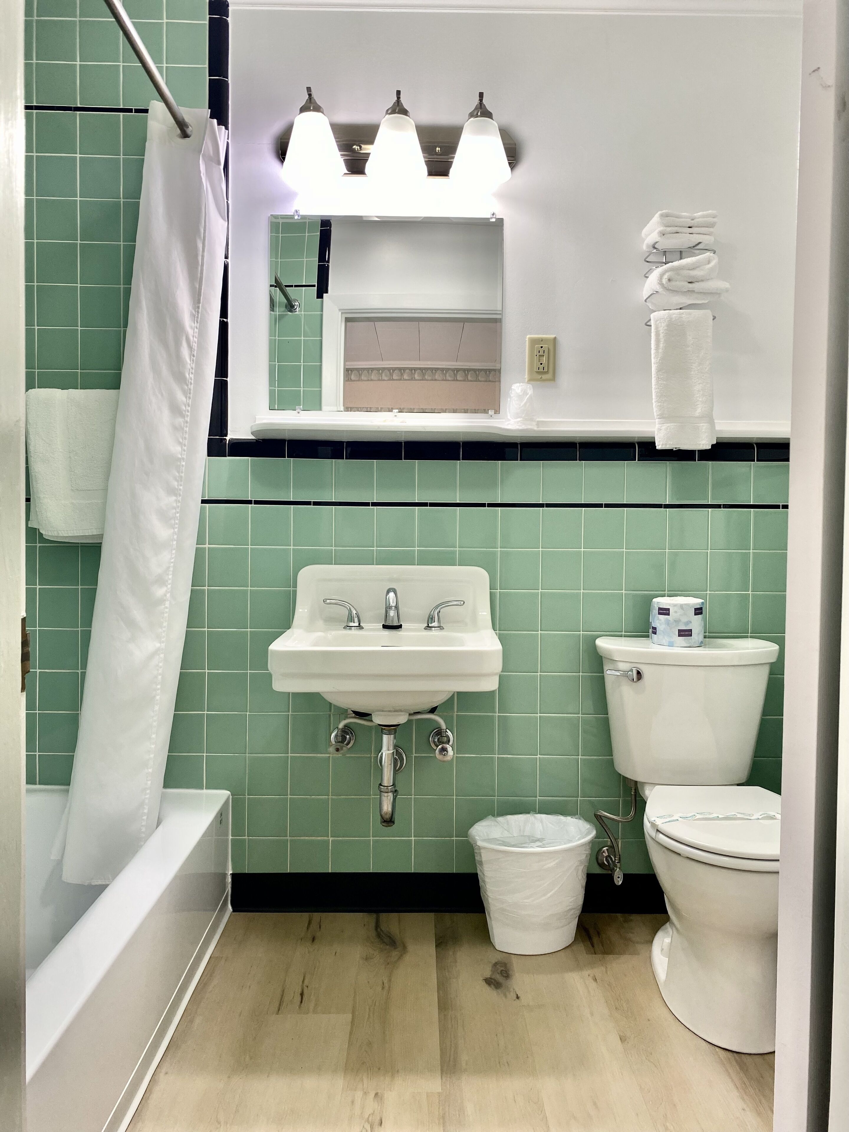 Une salle de bain avec un lavabo, des toilettes et une baignoire. Il y a trois lampes au-dessus du miroir et un porte-serviettes avec plusieurs serviettes.
