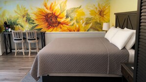 A bedroom with a large bed, a desk with chairs, and a wall mural of sunflowers.