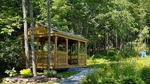 A wooden gazebo with a covered porch, surrounded by lush greenery and trees.