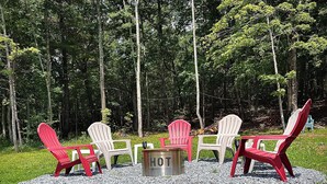 A seating area with Adirondack chairs and a metal table in a forest setting.