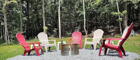 A seating area with Adirondack chairs and a metal table in a forest setting.