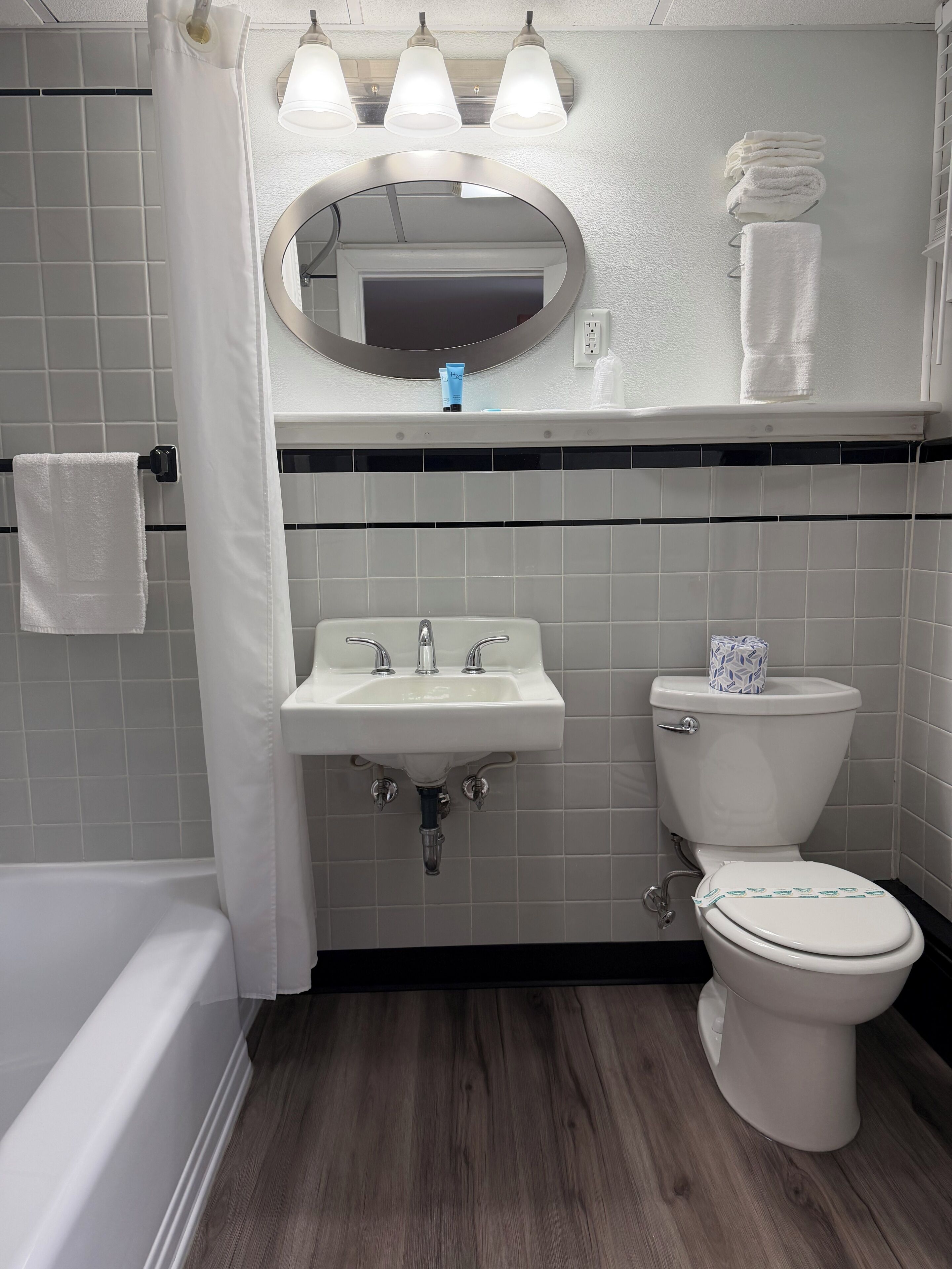A bathroom with a sink, toilet, and bathtub. There are three lights above the mirror, and a towel rack with towels.